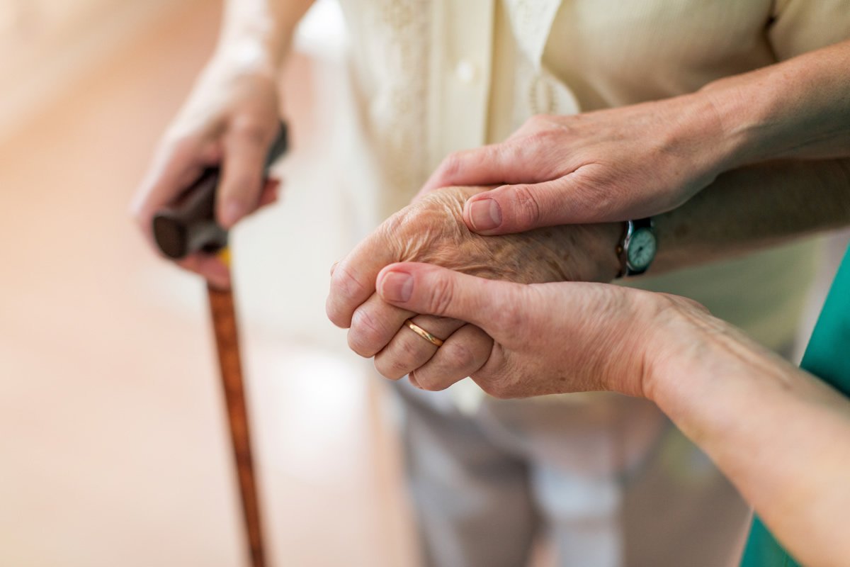 hands guiding elderly woman with a cane